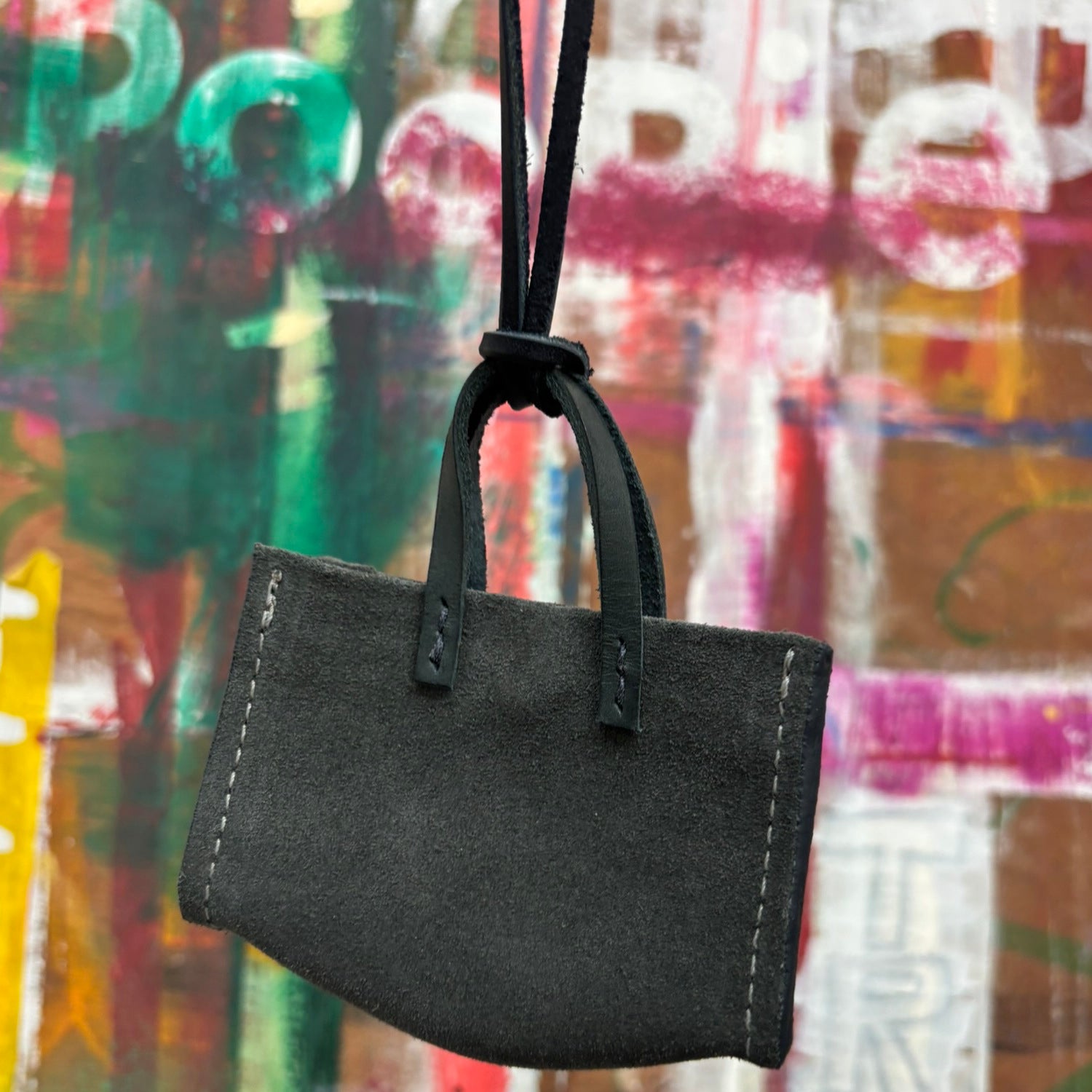 mini blue grey suede handbag with a strap against a colorful, abstract background